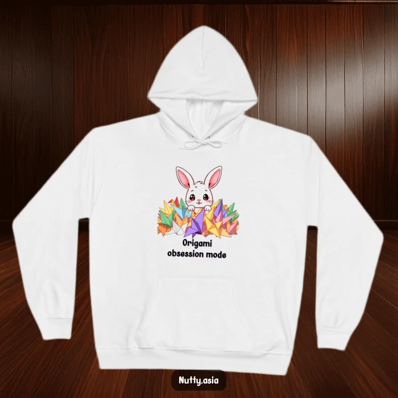 Funny hoodie depicting a cute bunny peeking with curiosity from a pile of colorful origami cranes, conveying adorable mischief.